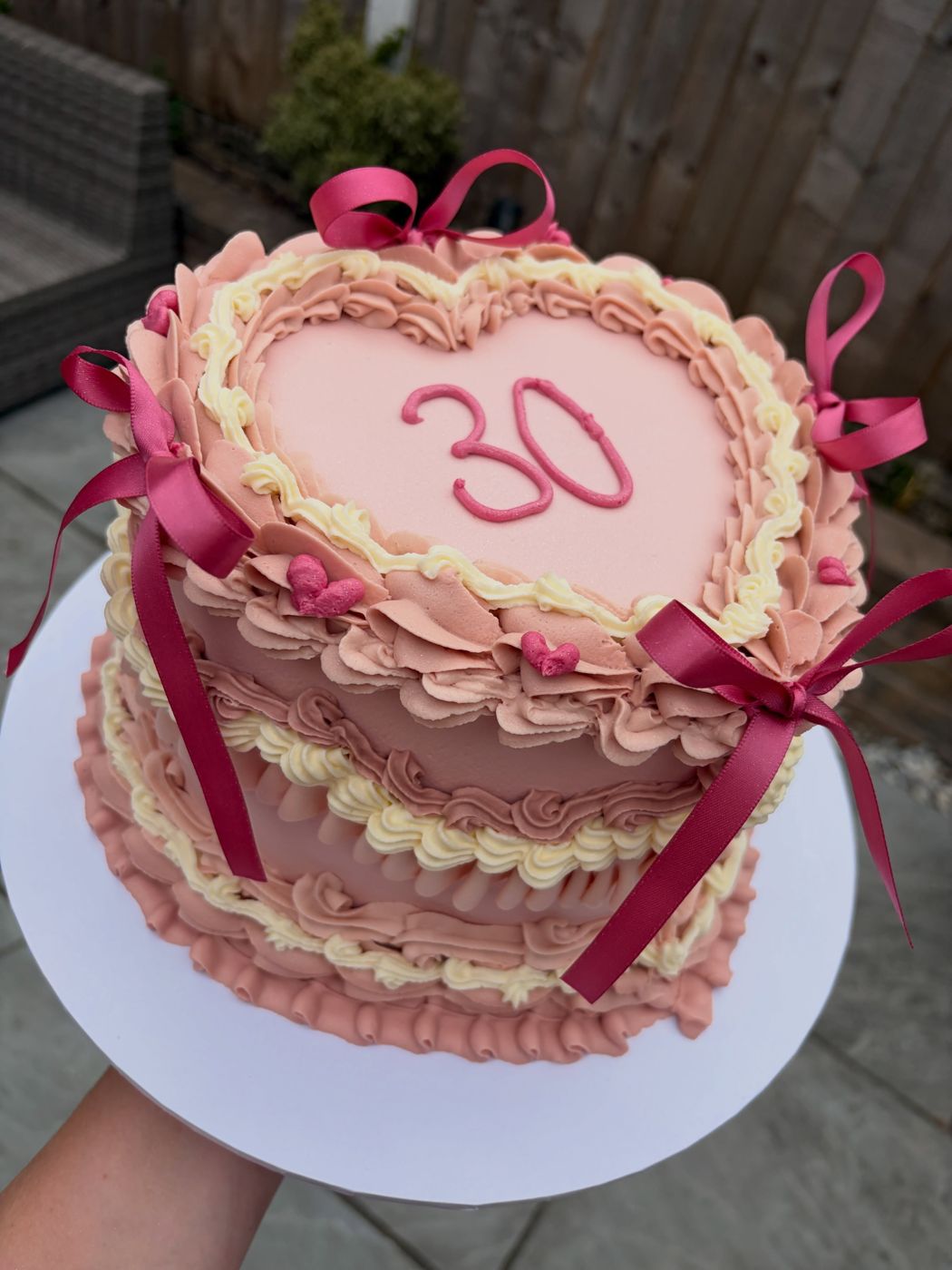 A heart-shaped vintage piped cake in pinks with burgundy bows and a piped 30