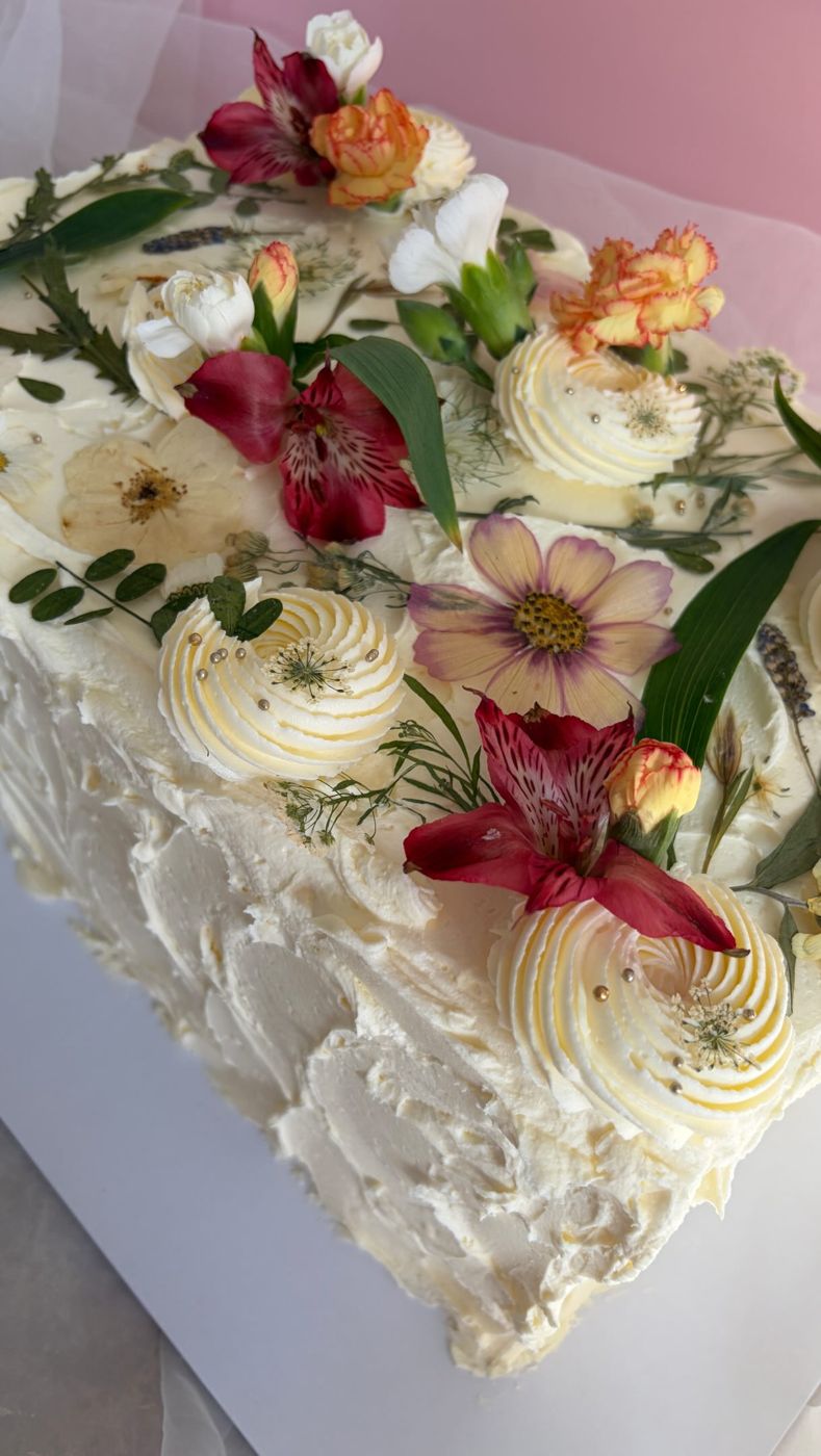 A white wedding cake dressed with burgundy and blush fresh flowers